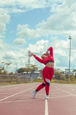 Joven afro de cabello naranja bailando al estilo urbano en parque local en la pista de atletismo, vejetaryen y cielo hermosos de fondo