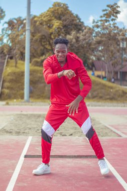 Joven afro bailando al estilo urbano en un parque, con hermosa veacion y cielo de fondo