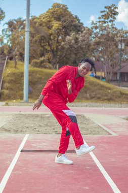 Joven afro bailando al estilo urbano en un parque, con hermosa veacion y cielo de fondo