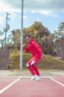 Joven afro bailando al estilo urbano en un parque, con hermosa veacion y cielo de fondo