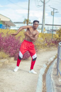 Joven afro bailando al estilo urbano sin camiseta, con hermosa veacion y cielo de fondo