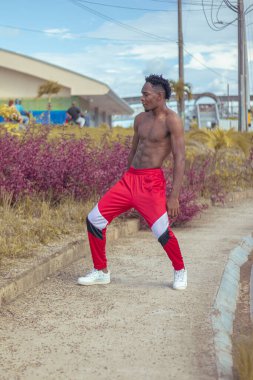 Joven afro bailando al estilo urbano sin camiseta, con hermosa veacion y cielo de fondo