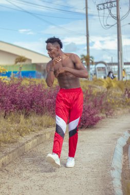 Joven afro bailando al estilo urbano sin camiseta, con hermosa veacion y cielo de fondo