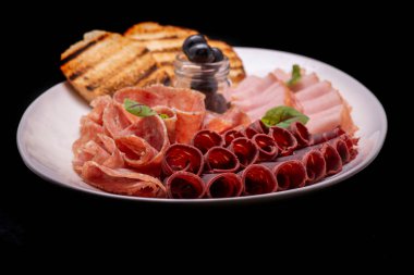 Dilimlenmiş füme sosis ve siyah arka planda karabiber, sarımsak ve biberiye.