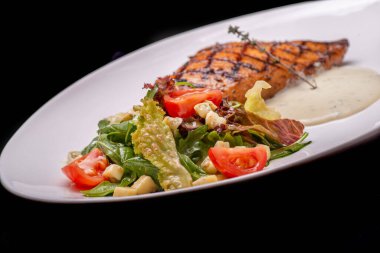 Lezzetli ızgara balık ve siyah tabakta taze sebze. Sağlıklı yemek. Kapat.