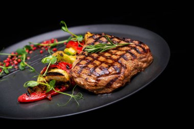 Siyah arka planda sebzeli ızgara biftek ve otlar.