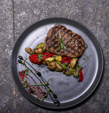 Biberiyeli ızgara biftek ve siyah arka planda siyah bir tabakta kiraz domatesleri..