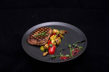 Izgara sebzeli biftek ve siyah arka planda siyah tabakta et. Yemek ve yemek konsepti. Metnin için kopyalama alanı olan üst görünüm.