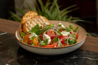 Salata ahşap bir masada domates, peynir ve otlarla..