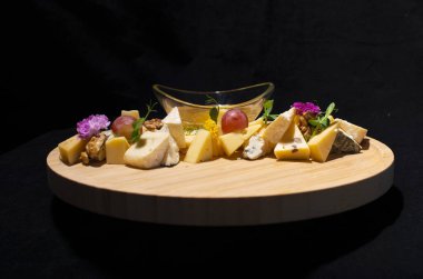 Ballı, peynirli ve otlu ahşap tepside siyah bir arka planda