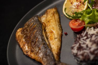 Patatesli fırında balık filetosu, kırmızı balık filetosu, siyah tabakta taze sebzeler, üst manzara.