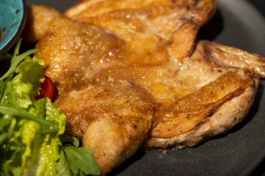 Baharatlı tavuk budu ve siyah bir tabakta otlar.