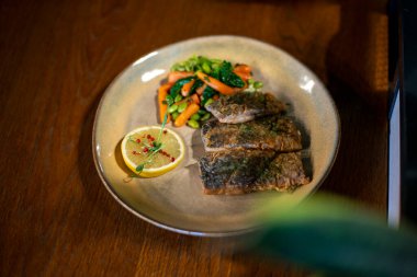 Tahta bir masada limonlu kızarmış balık ve otlar.