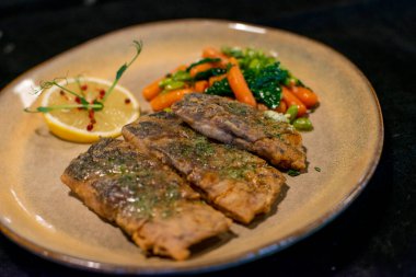 Ahşap masada sebzeli ızgara alabalık bifteği.