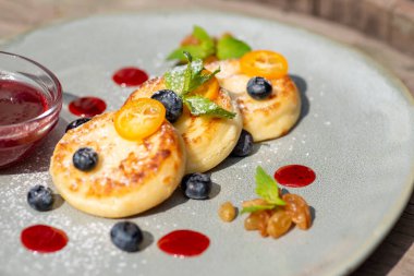 Böğürtlenli süzme peynir krepleri ve siyah ahşap arka planda bir tabakta şırınga. Sağlıklı yemek. Kahvaltı.