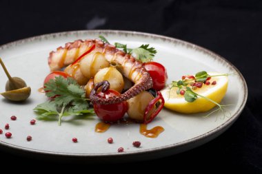 Izgara deniz tarağı, patates, limon, otlar ve baharatlar siyah tabakta.