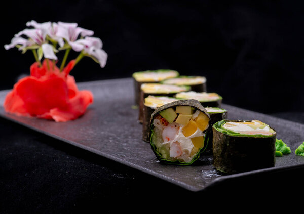японские роллы с лососем и овощами на черной каменной тарелке