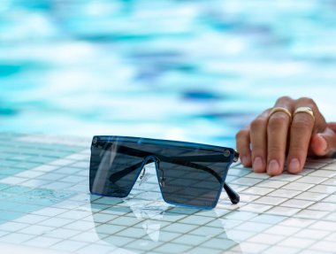 Yüzme havuzunun arka planında güneş gözlüğü ve yüzme gözlükleri