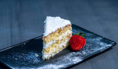 Kremalı ve çilekli pasta siyah masada, kapat.