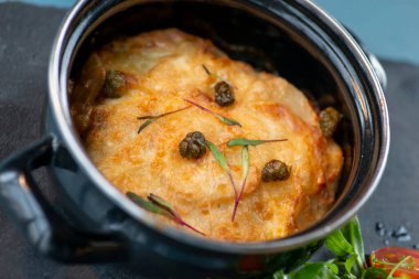 Siyah bir masada tavuk göğsü ve peynirli güveç.