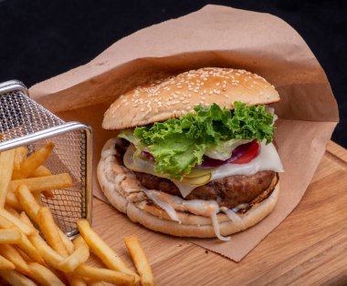 Lezzetli hamburger, patates kızartması ve peynirli siyah ahşap tabakta siyah masa, fast food.