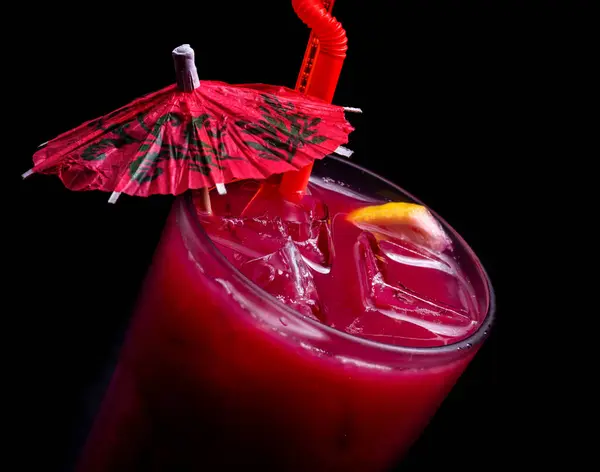 a glass of red cocktail with cherry and ice on a black background