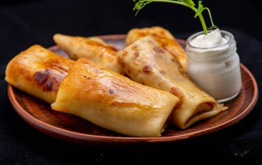 Ekşi kremalı krepler ve siyah bir tabakta beyaz bir arka planda otlar..