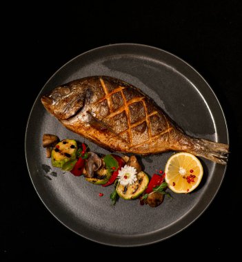 Limonlu ızgara levrek ve siyah arka planda otlar.