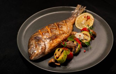 Siyah arka planda sebzeli ızgara balık.