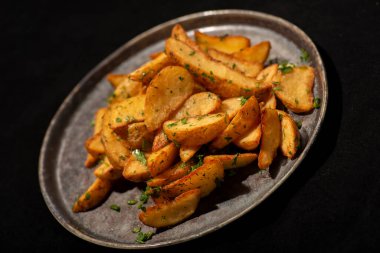 Patatesler siyah tabakta, siyah arka planda.