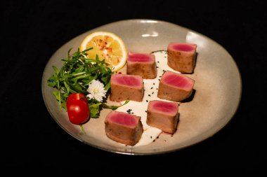 Tahta yüzeyde siyah tabakta salatalı ton balığı bifteği.