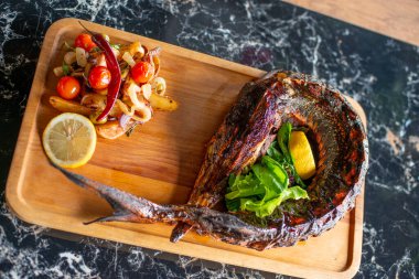 Kızarmış domuz pirzolası, limonlu ve sebzeli ve ahşap masadaki otlarla servis ediliyor.