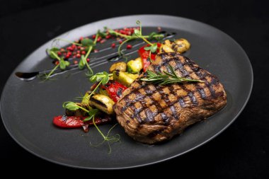 Siyah arka planda sebzeli ızgara biftek.