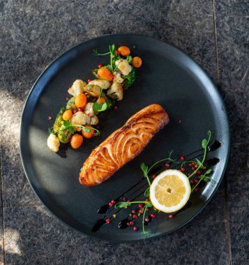 Sebzeli somon filetosu ve siyah tahta tabakta otlar..