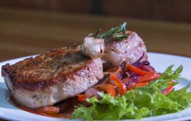 Sebzeli kızarmış biftek ve masada beyaz bir tabakta yeşillikler..