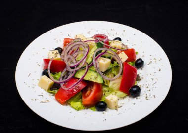 Taze sebzeli salata, siyah arka planda beyaz tabakta beyaz peynir.