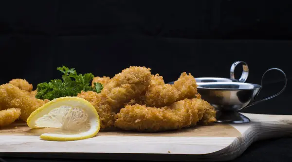 breaded chicken breast with lemon, parsley, garlic, and lemon. on a dark background, close up