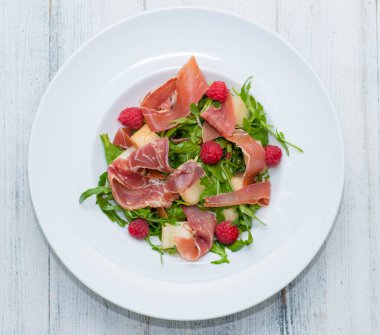 Tahta zemin üzerinde prosciutto olan roka salatası..