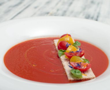 Tahta masada beyaz tabakta servis edilen domates çorbası.