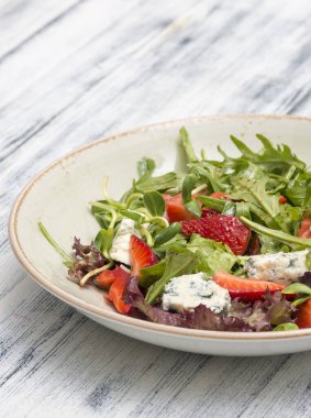 Beyaz tabakta roka, domates, ceviz ve peynirli nefis salata.