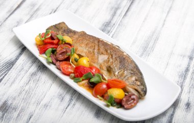 Beyaz tabakta sebzeli ve domatesli fırında balık. en üstteki görünüm