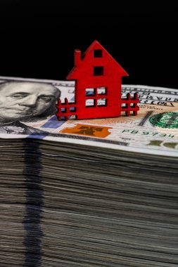 100 dolarlık banknotların üzerinde minyatür kırmızı bir ev duruyor..
