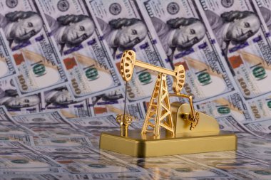 A miniature gold oil pump against the background of 100 US dollar bills