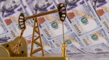 A miniature gold oil pump against the background of 100 US dollar bills