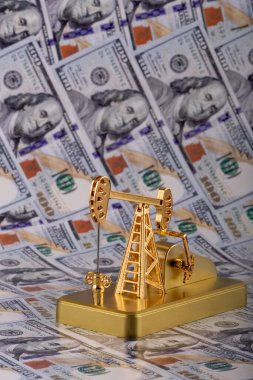 A miniature gold oil pump against the background of 100 US dollar bills