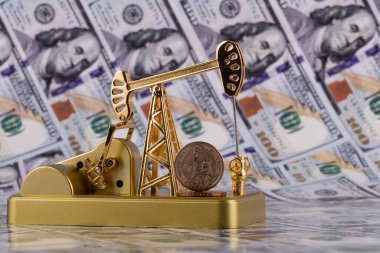 A gold miniature oil pump and a US$1 coin against a US$100 bill
