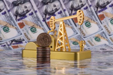 A gold miniature oil pump and a US$1 coin against a US$100 bill