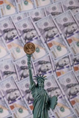 Statue of Liberty with a coin of 1 US dollar on the background of bills in denominations of 100 US dollars
