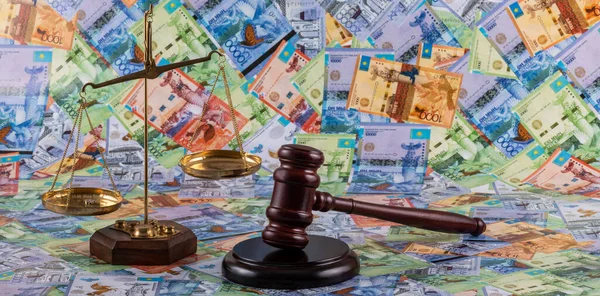 Judge's gavel and golden scales against the background of Kazakhstani banknotes - tenge
