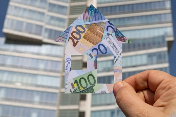 A symbolic house depicting euro banknotes of various denominations against the background of a modern building